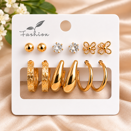 A set of gold-toned earrings displayed on a white card with the word 'Fashion' printed at the top. The set includes two round gold studs, two clear crystal stud earrings, two flower-shaped gold earrings, two textured gold hoop earrings, and two smooth gold hoop earrings.